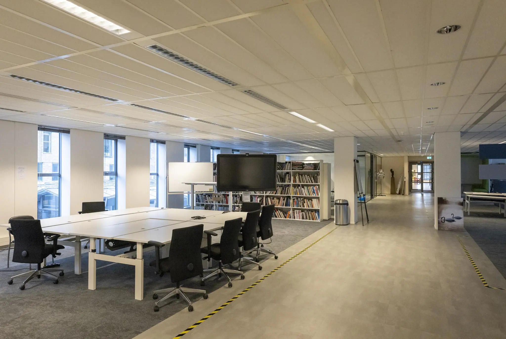 Moderne kantoorruimte aan de Prinses Beatrixlaan met vergadertafels, boekenkasten en een groot presentatiescherm.